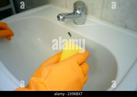 Reinigung und Desinfektion des Badezimmers in Nahaufnahme. Hände in hellen Latexhandschuhen auf dem gefliesten Waschbecken halten einen Schwamm. Stockfoto