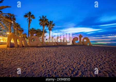 Strand in Malaga Spanien mit einem Malagueta Strand Schild. Ein Málaga-Strand mit Panoramablick auf die Skyline mit blauem Himmel und leichten Wegen bei Sonnenuntergang, Dämmerung, keine Leute. Stockfoto