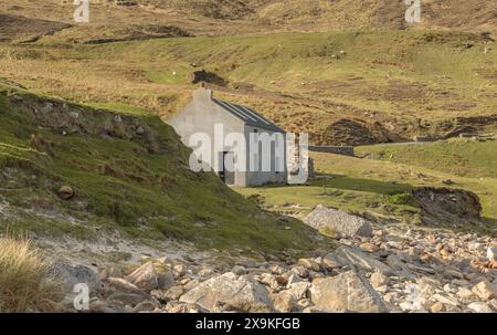 Graues Gebäude an einer Küste aus Felsen und Steinen vor einer Bergkulisse Stockfoto