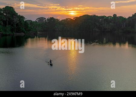 Einheimischer Quechua-Mann, der bei Sonnenaufgang Kanu reitet, Amazonas Regenwald, Yasuni-Nationalpark, Ecuador. Stockfoto