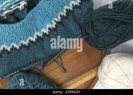 Close-up Flat Lay-Fotografie eines türkisweißen Wollgarns, das auf einer Holznadeln mit Garnkugeln strickt, Stockinette-Stich gestrickte Textur im Programm Stockfoto