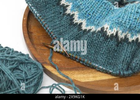 Close-up Flat Lay Fotografie eines türkisweißen Wollgarns, das auf einer Holznadel mit Garnkugeln gestrickt wird, Stockinette-Naht gestrickte Textur in Progre Stockfoto