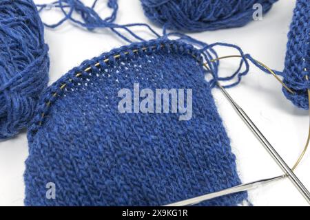 Close-up Flat Lay Fotografie eines blauen Wollgarns, das auf einer Metallnadel mit Garnkugeln auf weißem Hintergrund gestrickt wird, Stockinette-Naht gestrickte Textur Stockfoto