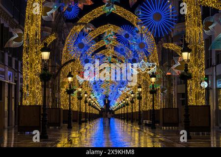 Karneval in Malaga, Spanien. Nicht erkennbare Menschen, die die Larios Straße in der Nähe des Constitution Square in der Altstadt von Malaga mit Weihnachtslichtern bei Nacht hinunterlaufen Stockfoto