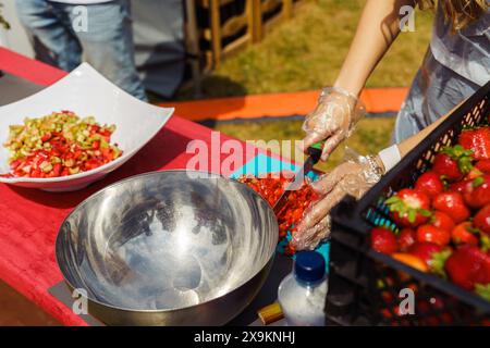 Hände einer Frau in Einweghandschuhen, die reife Erdbeeren würfelt, um Marmelade, Marmelade oder Kuchen im Garten zu machen. Der Prozess des Kochens von Sommergerichten mit frischen Stockfoto
