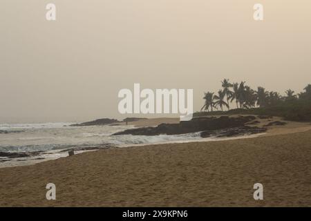 Ein felsiger Strand bei Sonnenuntergang, mit Wellen, die gegen die Felsen krachen. Der Himmel ist eine Mischung aus warmen Farbtönen, die ein goldenes Leuchten über die Szene zaubern und ein s erzeugen Stockfoto