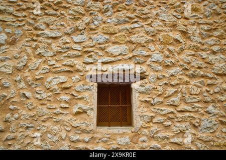 Beige Steinmauerwand aus Sandstein mit Fenster mit Holzsturz und Sicherheitsgrill aus Metall. Solche Mauern sind auf Mallorca, Spanien üblich Stockfoto