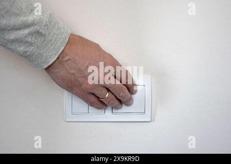 Die männliche Hand drückt die Taste des weißen Schalters, der an der Lichtwand montiert ist. Nahaufnahme. Selektiver Fokus. Kopierbereich. Stockfoto