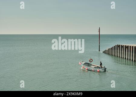Ein Fischer führt an klaren Tagen ein kleines Fischerboot aus dem Hafen von West Bay in Dorset in das englische Ärmelkanalmeer Stockfoto