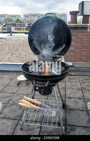 Black Compact Holzkohlegrill Wasserkocher mit gebratenem Gemüse auf der Terrasse, im Garten oder auf dem Dach. Stockfoto