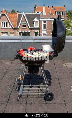 Black Compact Holzkohlegrill Wasserkocher mit gebratenem Gemüse auf der Terrasse, im Garten oder auf dem Dach. Stockfoto