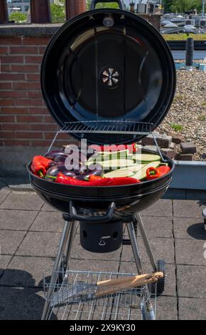 Black Compact Holzkohlegrill Wasserkocher mit gebratenem Gemüse auf der Terrasse, im Garten oder auf dem Dach. Stockfoto