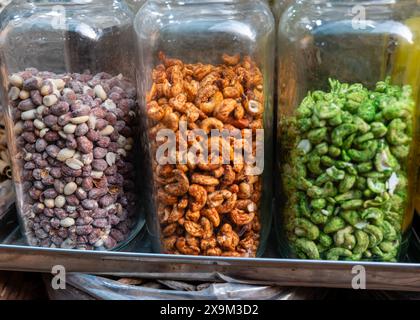 Drei Glasgläser sind mit einer Auswahl an Masala-Nüssen gefüllt – violett gesprenkelt, kräftig braun und leuchtend grün. Ein schmackhaftes Display für Lebensmittel Stockfoto