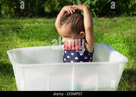 Ein Baby, das draußen in einem Garten in einer Plastikwanne steht, ein Hemd mit Herzmuster trägt und die Arme streckt, Weißrussland, Minsk Stockfoto