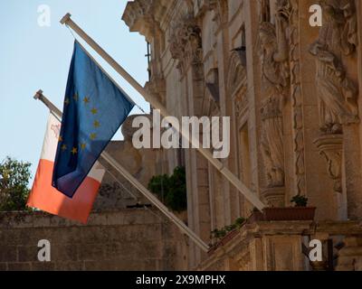 Zwei Flaggen, eine der EU und eine von Malta, vor der historischen Steinarchitektur, die Stadt mdina auf der Insel malta mit historischen Häusern Stockfoto