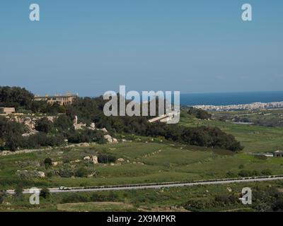 Riesige grüne Landschaft mit Hügeln, Bäumen und einer Stadt am Horizont unter klarem Himmel, die Stadt mdina auf der Insel malta mit historischen Häusern Stockfoto