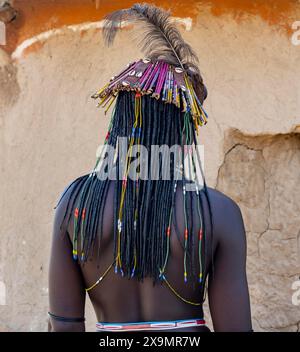 Hakaona-Frau mit traditioneller Kapapo-Frisur und Haarschmuck mit Straußenfedern und farbenfrohen Halsketten von hinten im Morgenlicht Stockfoto