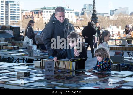 Ein Vater und zwei Kinder stöbern durch die Bücher des Southbank Book Market unter freiem Himmel an der Themse, London. Junge hält Eisbecher. Stockfoto