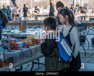 Ein Junge in der Hand eines Eiskegels und ein Mädchen stöbern im Southbank Book Market an der Themse in London unter freiem Himmel durch Kinderbücher. Stockfoto