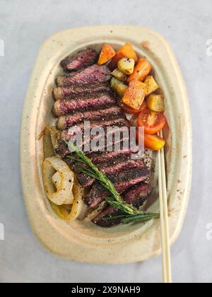 Ribeye-Steak, mittelselten auf Teller gekocht, mit Gemüse einschließlich Karotten und Zwiebeln, verzehrfertig, Schuss von oben Stockfoto