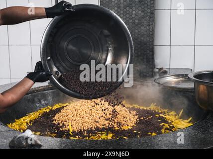 Die Hände des Küchenchefs geben Rosinen in einen Kessel mit Kichererbsen und gelben Karotten, um usbekische Pilaw in einem Restaurant in Taschkent in Usbekistan zu kochen Stockfoto