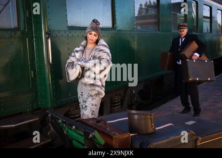 Nachstellungsszene auf dem Bahnsteig in der Nähe eines authentischen 1927 First Class Zugwaggons, wo eine schicke 1920er Dame auf ihr Gepäck wartet Stockfoto