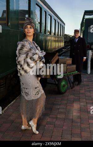 Nachstellungsszene auf dem Bahnsteig in der Nähe eines authentischen 1927 First Class Zugwaggons, wo eine schicke 1920er Dame auf ihr Gepäck wartet Stockfoto