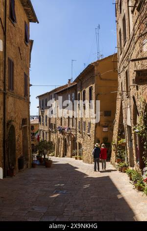 Zwei Touristen, die an einem sonnigen Tag die atemberaubende Aussicht auf eine wunderschöne, enge Straße in der historischen mittelalterlichen Altstadt von Volterra in der Toskana, Italien, bewundern. Stockfoto