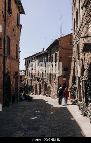 Zwei Touristen, die an einem sonnigen Tag die atemberaubende Aussicht auf eine wunderschöne, enge Straße in der historischen mittelalterlichen Altstadt von Volterra in der Toskana, Italien, bewundern. Stockfoto