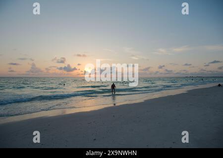 Sonnenuntergang am Pass-a-Grille Beach in St. Petersburg Florida. Schwaches Licht mit mehreren Personen im Wasser. Goldenes Leuchten und blauer Himmel der Sonne horizontal Stockfoto