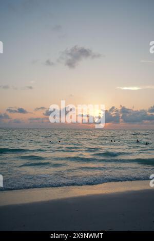 Sonnenuntergang am Pass-a-Grille Beach in St. Petersburg Florida. Schwaches Licht mit mehreren Personen im Wasser. Goldenes Leuchten und blauer Sonnenhimmel hinten. Stockfoto