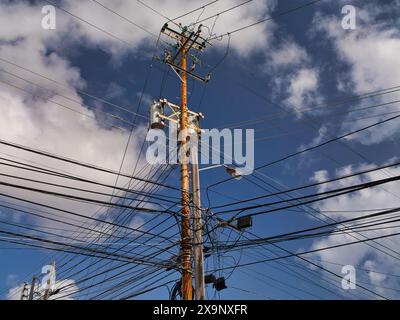 Tobago - 2. Februar 2024: Viele elektrische Kabel sind mit einem hölzernen Versorgungsmast auf der Insel Tobago in der Karibik verbunden. Gezeigt vor einem blauen Himmel mit Stockfoto