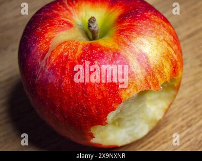 Frisch Gebissener Apfel. Ein roter Apfel mit einem Biss, der auf einer Holzoberfläche liegt und Themen der Gesundheit und Frische hervorruft. Stockfoto