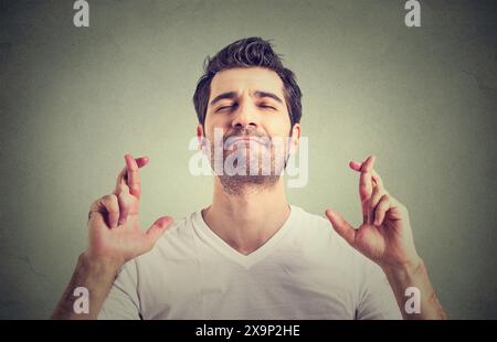 Der Mensch kreuzt die Finger, schließt die Augen und erwartet gute Nachrichten Stockfoto