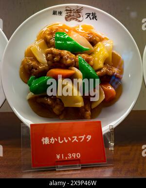 Lebhafte Darstellung von süß-saurem Schweinefleisch mit Gemüse und Sauce auf einer weißen Platte, Preise in japanischen Yen Stockfoto