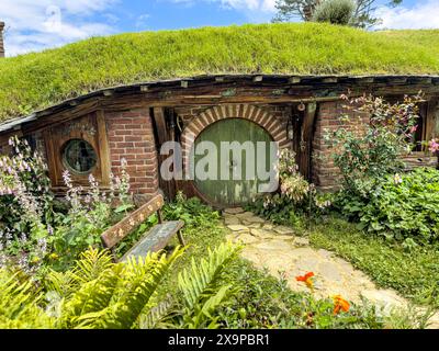 Gemütliches Hobbit-Haus am Hang mit grünem Dach und hölzerner Rundtür umgeben von üppigem Garten Stockfoto