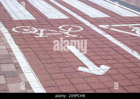 Die Abbildung zeigt einen weißen Pfeil auf einem Fahrradweg, der eine Rechtskurve anzeigt. Die Fahrbahn besteht aus Asphalt mit rechteckigem und gemauertem Boden Stockfoto