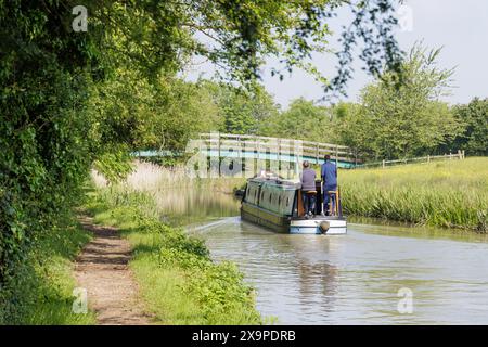 Northamptonshire, Großbritannien - Juni 2024: Zwei Männer stehen auf dem Heck eines Schmalbootes, während sie es durch die Landschaft entlang des Grand Union Canal segeln. Stockfoto