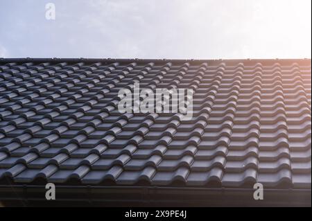 Der Close-up-Winkel eines modernen, schwarz gekachelten Dachs erfasst die detaillierte Struktur und die Kurven unter einem hellen Sonnenlicht und unterstreicht die moderne Architektur Stockfoto