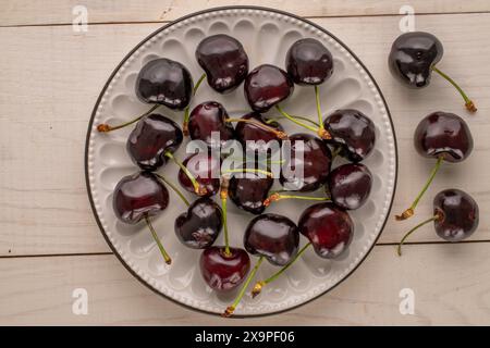 Mehrere reife süße Kirschen mit Keramikuntertasse auf Holztisch, Makro, Blick von oben. Stockfoto