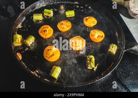 Gelbe Kirschtomaten und Spargel werden in einer gusseisernen Pfanne gebraten. Ausgewählter Fokus. Hochwertige Fotos Stockfoto