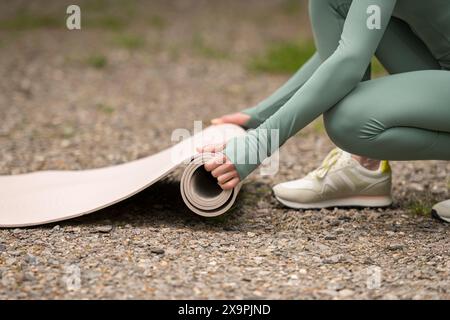 Nahaufnahme einer Frau, die Yoga-Matte nach dem Training im Park rollte. Gesunder Lebensstil. Fitnessgeräte, Pilates, Yoga. Wellbeing-Konzept. Stockfoto