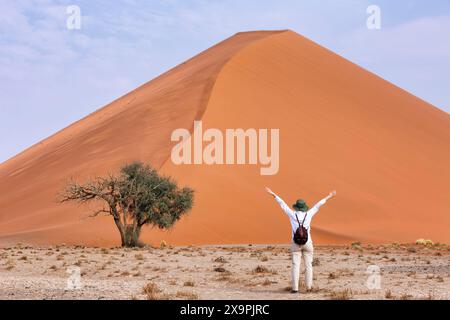 Junger Tourist mit den Armen hoch und Blick auf die Düne 45 in der Namib Naukluft Wüste, Namibia, Südafrika Stockfoto