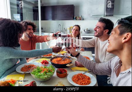 Glückliche Erwachsene Freunde, die Spaß haben, Rotwein zu trinken und zusammen zu essen. Multirassische Menschen beim Mittagessen - Hauptfokus auf Hände Stockfoto