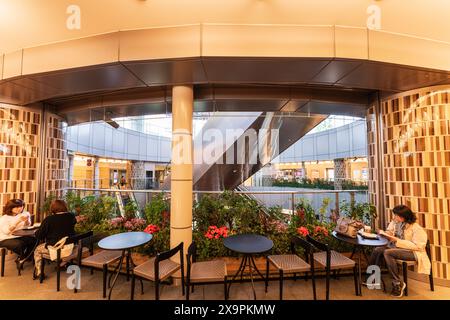 Sitze und Tische auf einem Balkon mit Blick auf die Rolltreppen, drei japanische Frauen trinken Kaffee im Metro hat Shopping Center in Roppongi Hills. Stockfoto