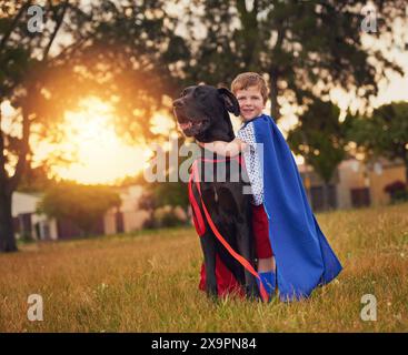 Porträt, Hund oder Kind mit Superheldenkostüm im Garten zum Umarmen, Binden und Spielen im Freien. Tiere, Haustier oder glücklicher Junge mit dem Welpen der Großen Däne im Park Stockfoto