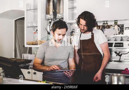 Gutaussehender Barista, der im Café arbeitet und mit dem Manager über Schichten und Arbeitszeitpläne spricht. Universitätsstudentin arbeitet Teilzeit im Café. Stockfoto