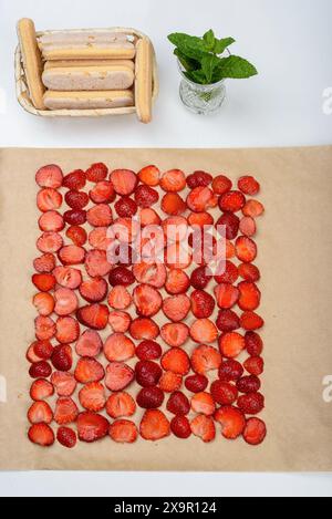 Reihen geschnittener Erdbeeren auf Backpapier. Tiramisu-Kuchen zuhause zubereiten. Stockfoto