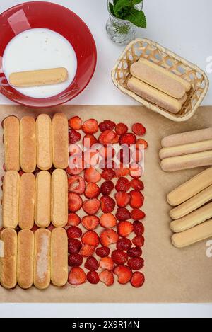 Weichen Sie die Savoiardi in Milch ein und legen Sie sie in Reihen auf die Erdbeeren. Bereiten Sie den Tiramisu-Kuchen zu Hause zu. Stockfoto