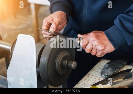 Hände eines männlichen, handwerklichen Schleifers, der die Messerklinge auf einer Schleifmaschine in Nahaufnahme schärft Stockfoto